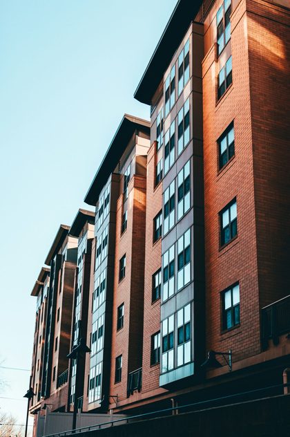 Façana d’un bloc d’habitatges de maó vermell amb finestres, sota un cel clar. Fotografia de Seyi Ariyo.